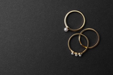 Elegant pearl rings on black background, flat lay. Space for text