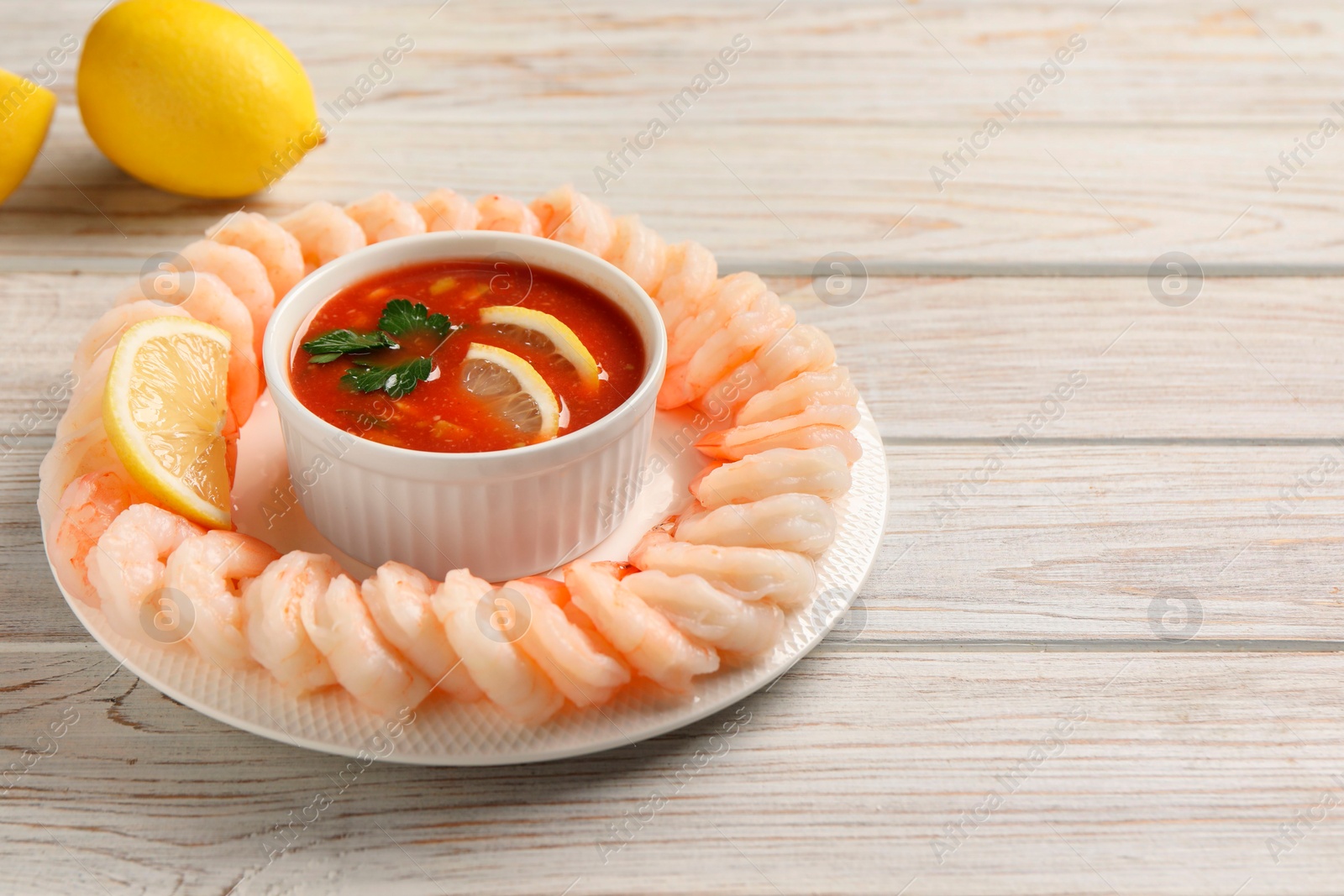Photo of Tasty boiled shrimps with cocktail sauce and lemon on white wooden table, space for text
