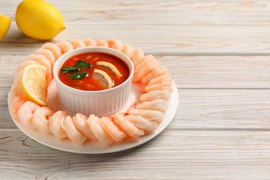 Tasty boiled shrimps with cocktail sauce and lemon on white wooden table, space for text