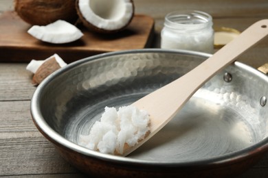 Photo of Frying pan with coconut oil and wooden spatula on wooden table, closeup. Healthy cooking