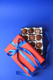 Photo of Box with delicious chocolate candies on blue background, top view