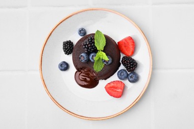 Plate with delicious chocolate fondant, berries and mint on white tiled table, top view