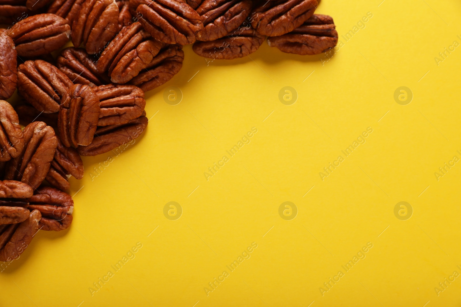 Photo of Heap of tasty nuts on yellow background, space for text