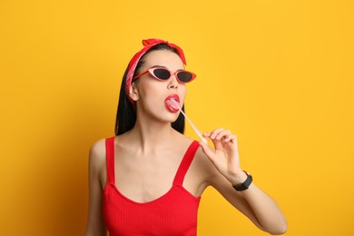 Fashionable young woman in pin up outfit chewing bubblegum on yellow background