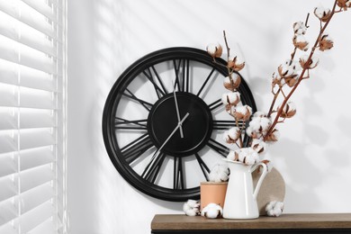 Photo of Cotton branches with fluffy flowers and home decor on wooden table near white wall. Space for text