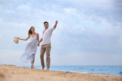 Happy couple having romantic walk on beach. Space for text