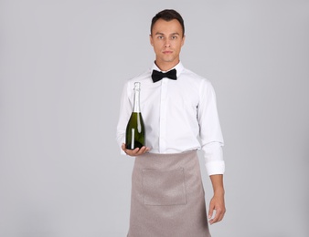 Photo of Waiter with bottle of champagne on grey background