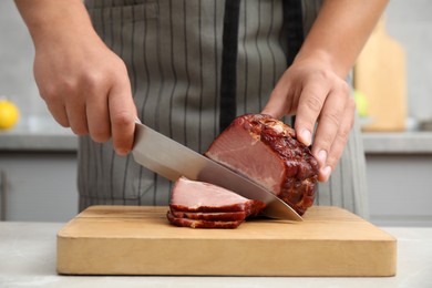 Photo of Man cutting ham on wooden board at table indoors, closeup