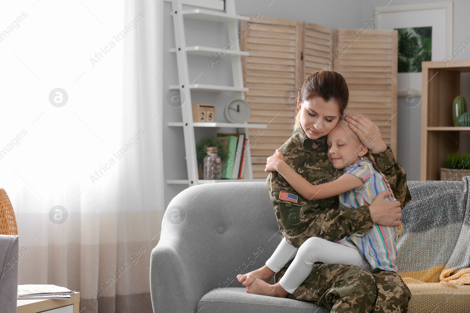 Photo of Woman in military uniform with her little daughter on sofa at home