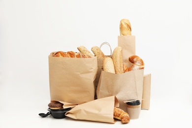 Different fresh bakery products in paper bags on white background