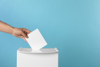 Man putting his vote into ballot box on light blue background, closeup. Space for text