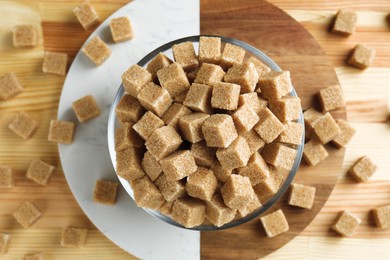 Photo of Brown sugar cubes in bowl on wooden table, top view