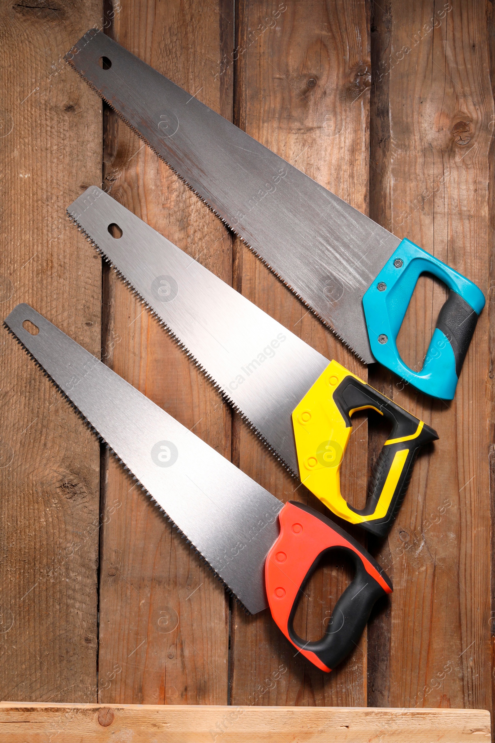 Photo of Saws with colorful handles on wooden surface, flat lay