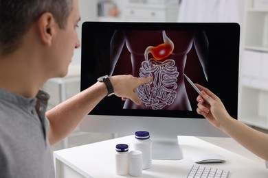 Gastroenterologist showing screen with illustration of digestive tract to patient at table in clinic, closeup