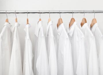 Photo of Rack with clean clothes after dry-cleaning on hangers in wardrobe