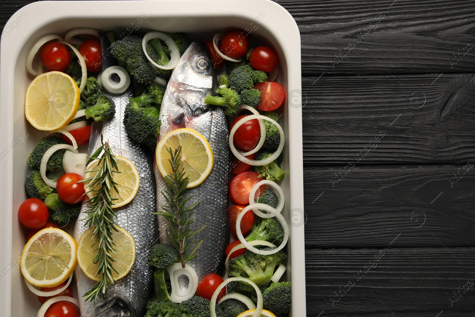 Photo of Raw fish with vegetables and lemon in baking dish on black wooden table, top view. Space for text