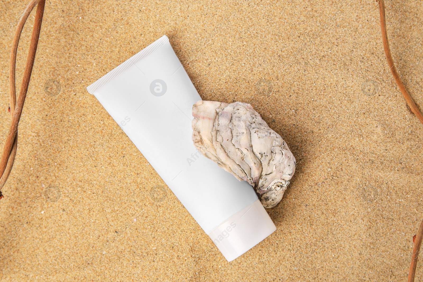 Photo of Tube with cream, shell and branches on sand, top view. Cosmetic product