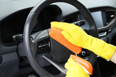 Photo of Woman cleaning steering wheel with rag in car, closeup