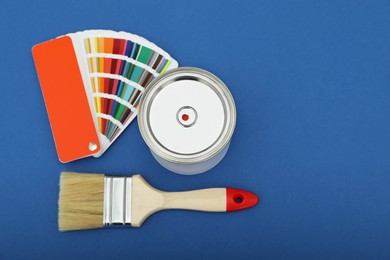 Photo of Can of orange paint, color palette samples and brushes on blue background. Space for text