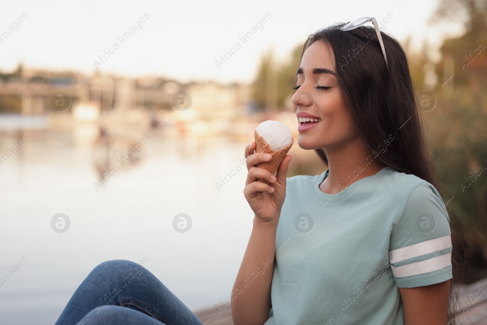 Photo of Happy young woman with delicious ice cream in waffle cone outdoors. Space for text