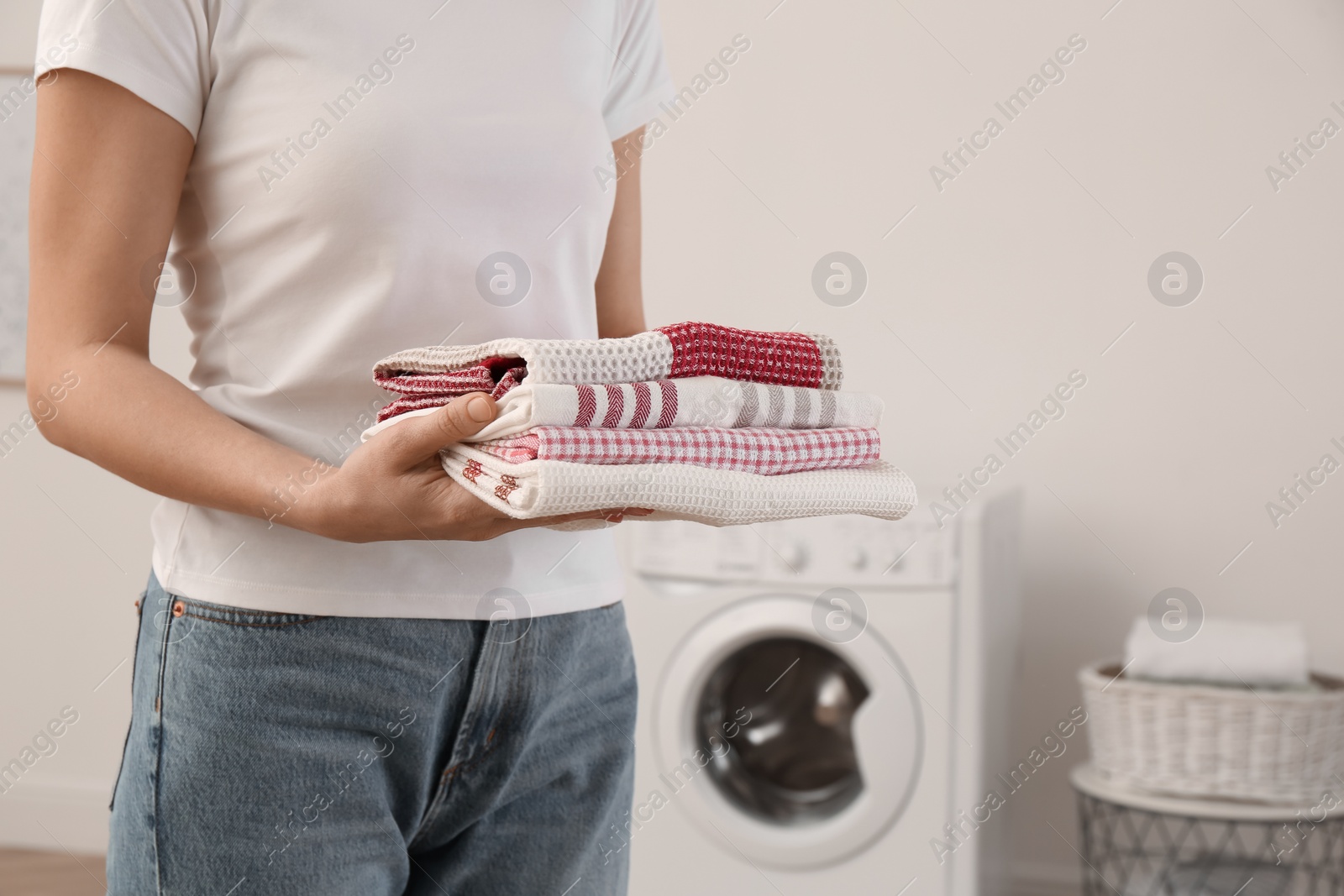 Photo of Woman with folded clean kitchen towels in laundry room, closeup