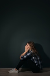 Photo of Depressed young woman sitting on floor in darkness