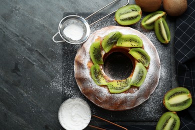 Photo of Homemade yogurt cake with kiwi and powdered sugar on black table, flat lay