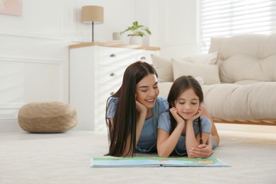 Young mother and her daughter reading book at home, space for text