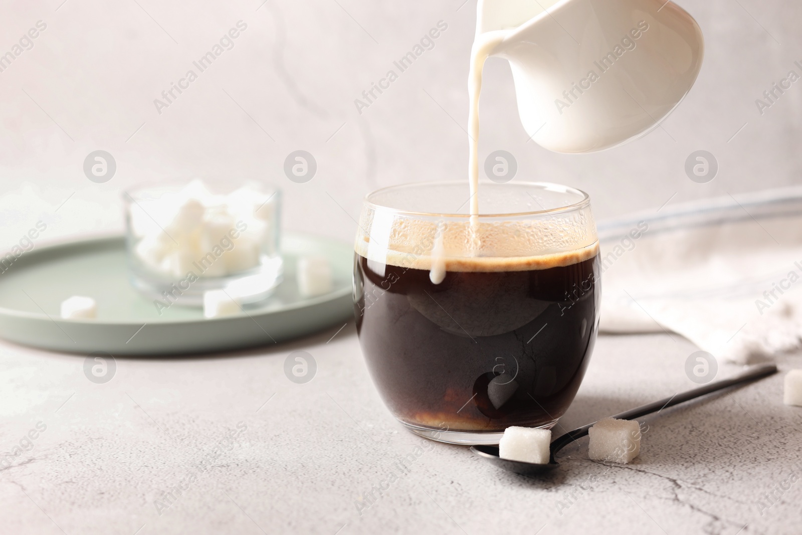 Photo of Pouring milk into cup with coffee on white textured table, closeup