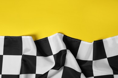 Photo of Checkered finish flag on yellow background, top view. Space for text