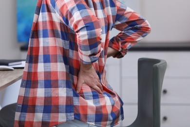 Photo of Young man suffering from back pain in office, closeup