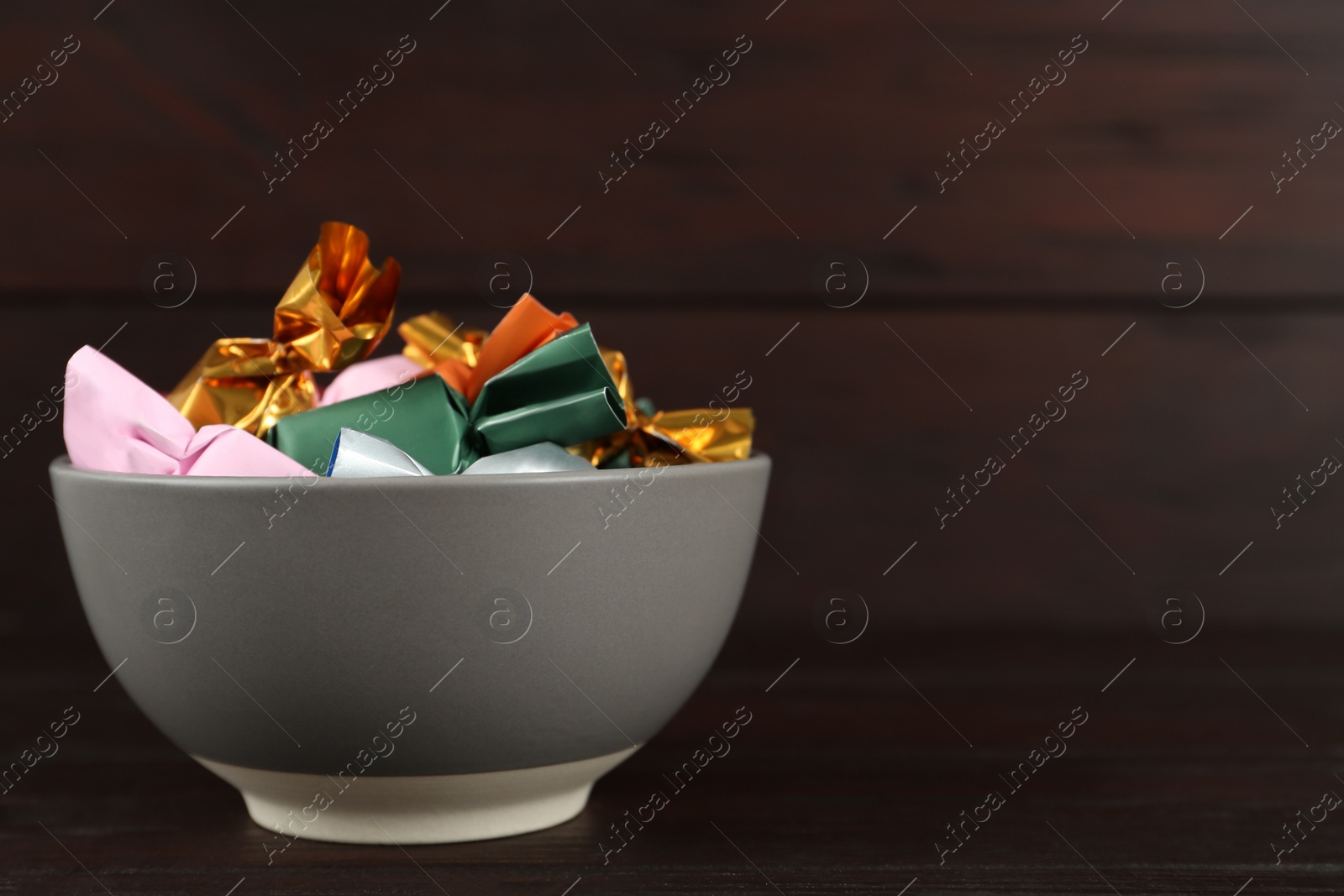 Photo of Candies in colorful wrappers on wooden table. Space for text