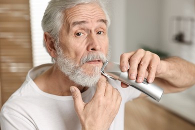 Senior man trimming mustache with electric trimmer in bathroom