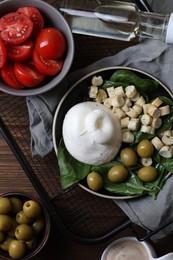 Photo of Delicious burrata cheese served with olives, croutons, basil and tomatoes on wooden table, top view