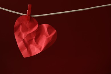 Photo of Crumpled red paper heart on rope against burgundy background, space for text. Broken heart