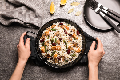 Photo of Woman with delicious rice pilaf at grey table, top view
