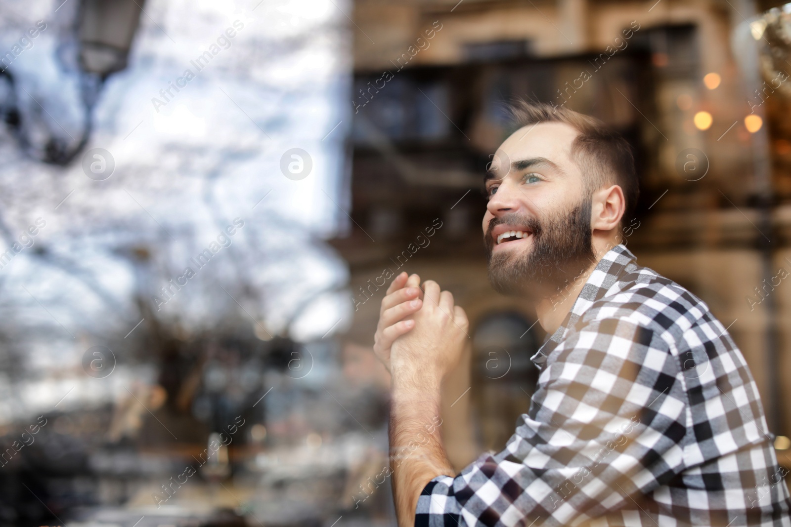 Photo of Handsome young man sitting in cafe, view from outdoors through window