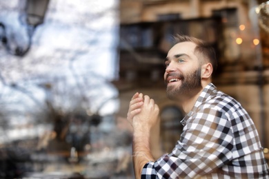 Handsome young man sitting in cafe, view from outdoors through window