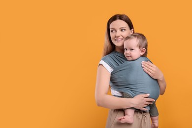 Mother holding her child in baby wrap on orange background. Space for text