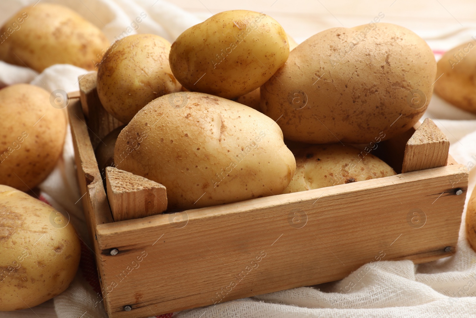 Photo of Raw fresh potatoes with crate on light wooden table, closeup