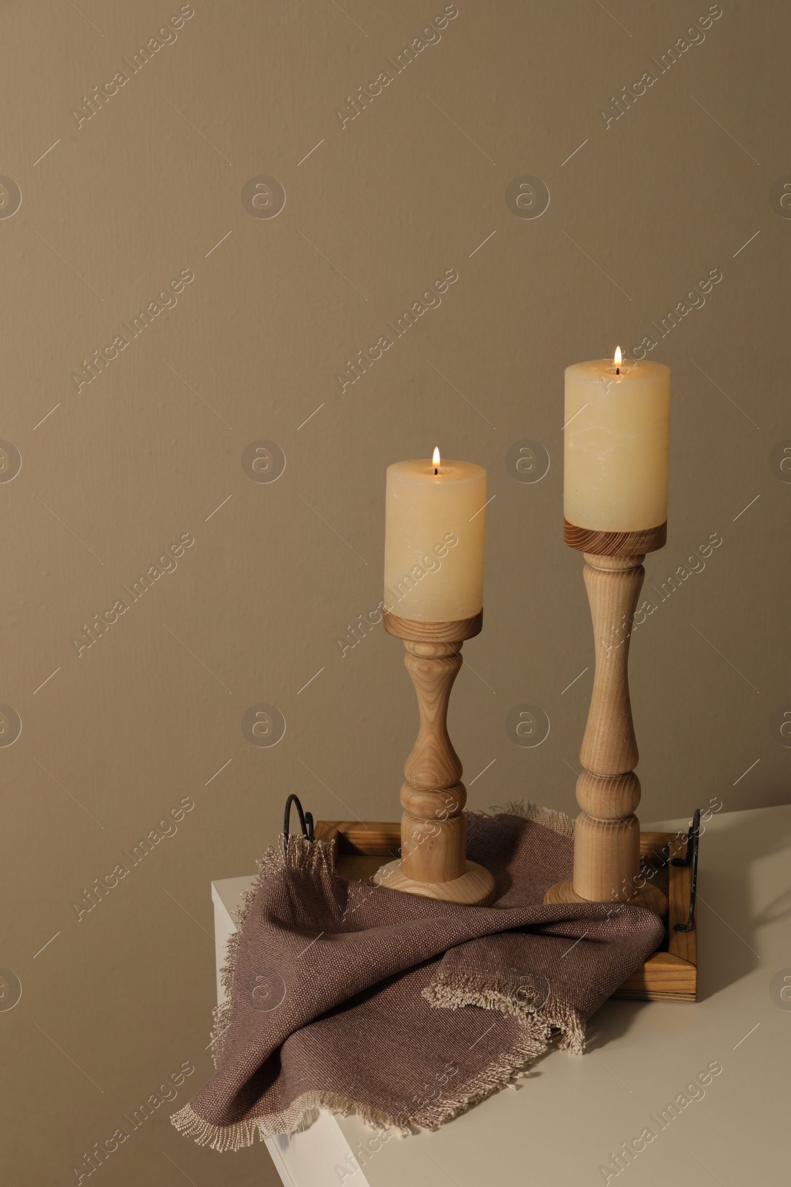 Photo of Holders with burning candles on white table near brown wall