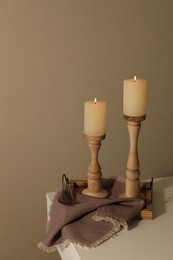 Holders with burning candles on white table near brown wall