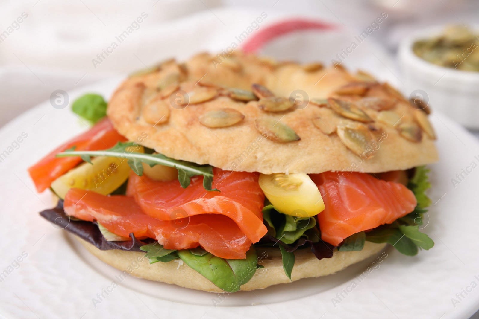 Photo of Tasty bagel with salmon and tomatoes on plate, closeup