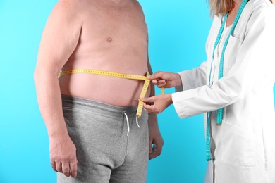 Photo of Doctor measuring senior man's waist on color background. Weight loss