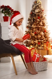 Photo of Cute little girl in Santa hat with gift from Christmas advent calendar at home