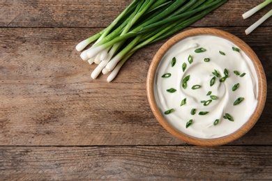 Photo of Bowl of fresh sour cream with green onion on wooden table, flat lay. Space for text