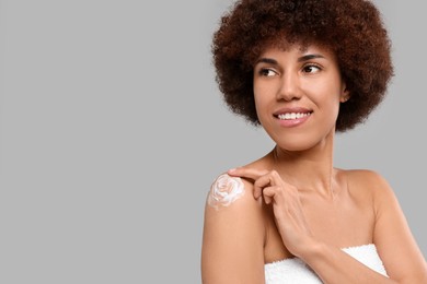 Photo of Beautiful young woman applying body cream onto shoulder on grey background, space for text