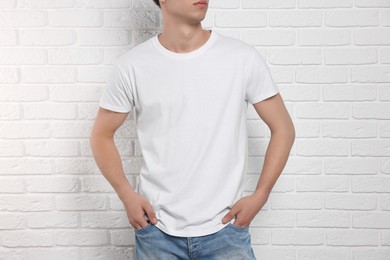 Photo of Man wearing stylish t-shirt near white brick wall, closeup. Mockup for design