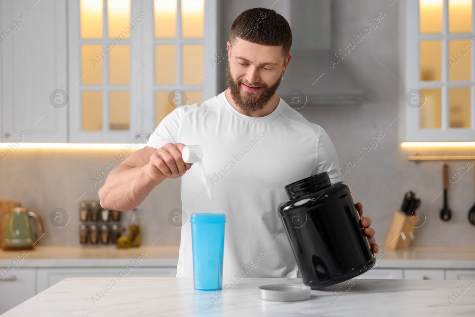 Photo of Young man making protein shake at white marble table in kitchen