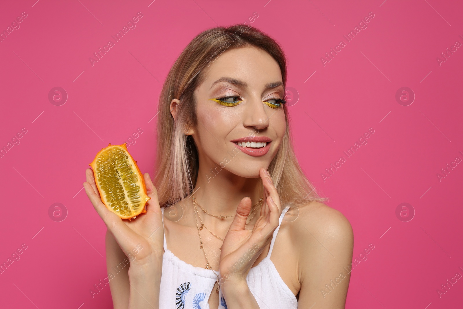 Photo of Young woman with fresh kiwano on pink background. Exotic fruit